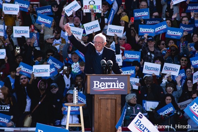 A smiling Bernie Sanders  lifts up his arm in acknowledgement of the crowd